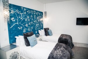 A modern bedroom with two beds, a blue wall art, a TV, and a small table.