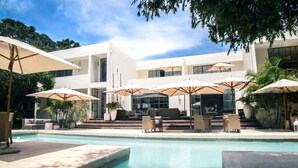 A pool area with lounge chairs and umbrellas, surrounded by a modern building with large windows. - Latitude 15 Degrees (Lusaka)