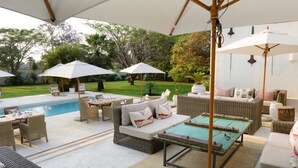 An outdoor patio area with a pool, wicker furniture, and umbrellas. - Latitude 15 Degrees (Lusaka)
