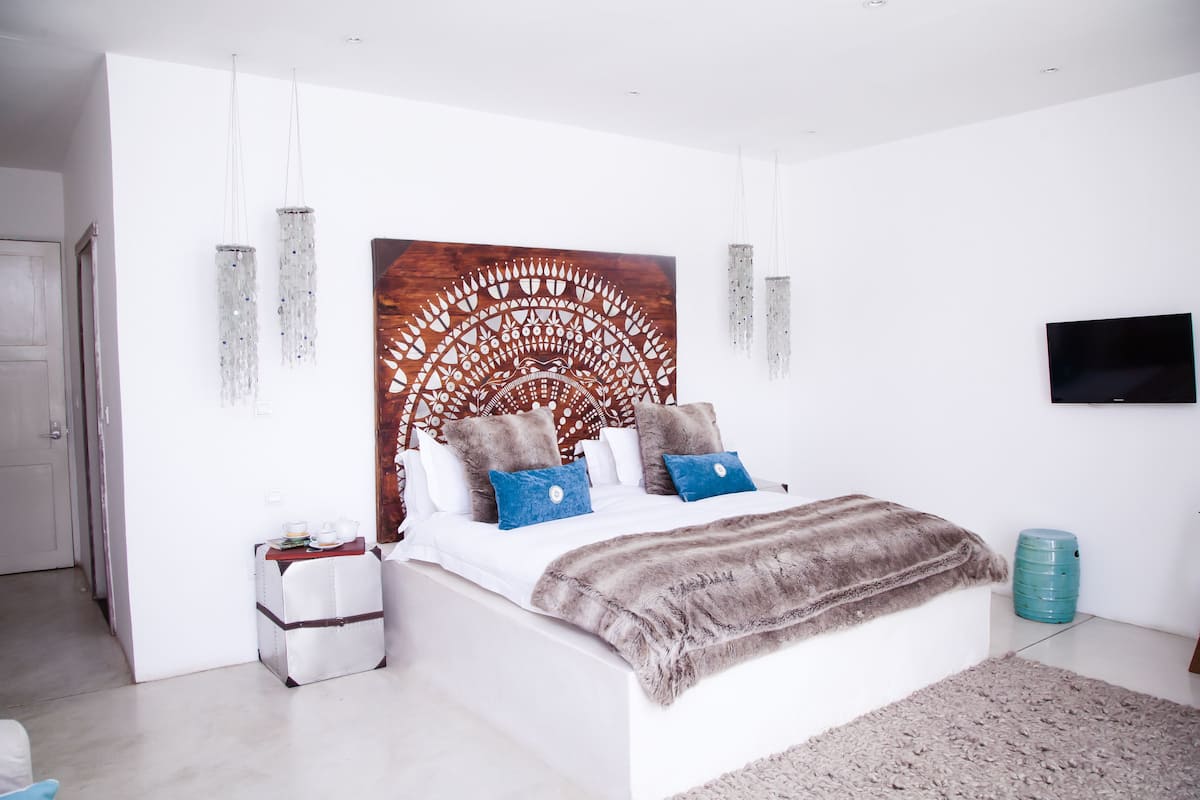 A modern bedroom with a large bed, a decorative headboard, a flat-screen TV, and a water dispenser.