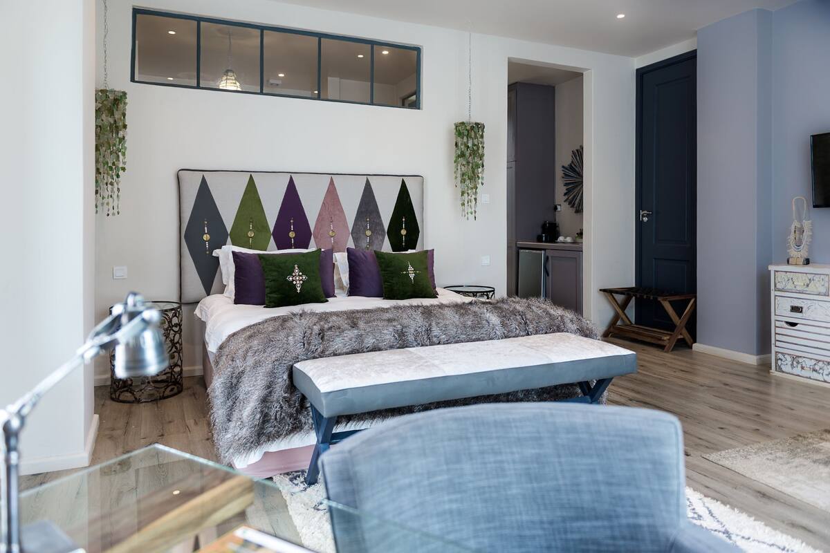A modern bedroom with a bed, a bench, a desk, and a hanging plant.