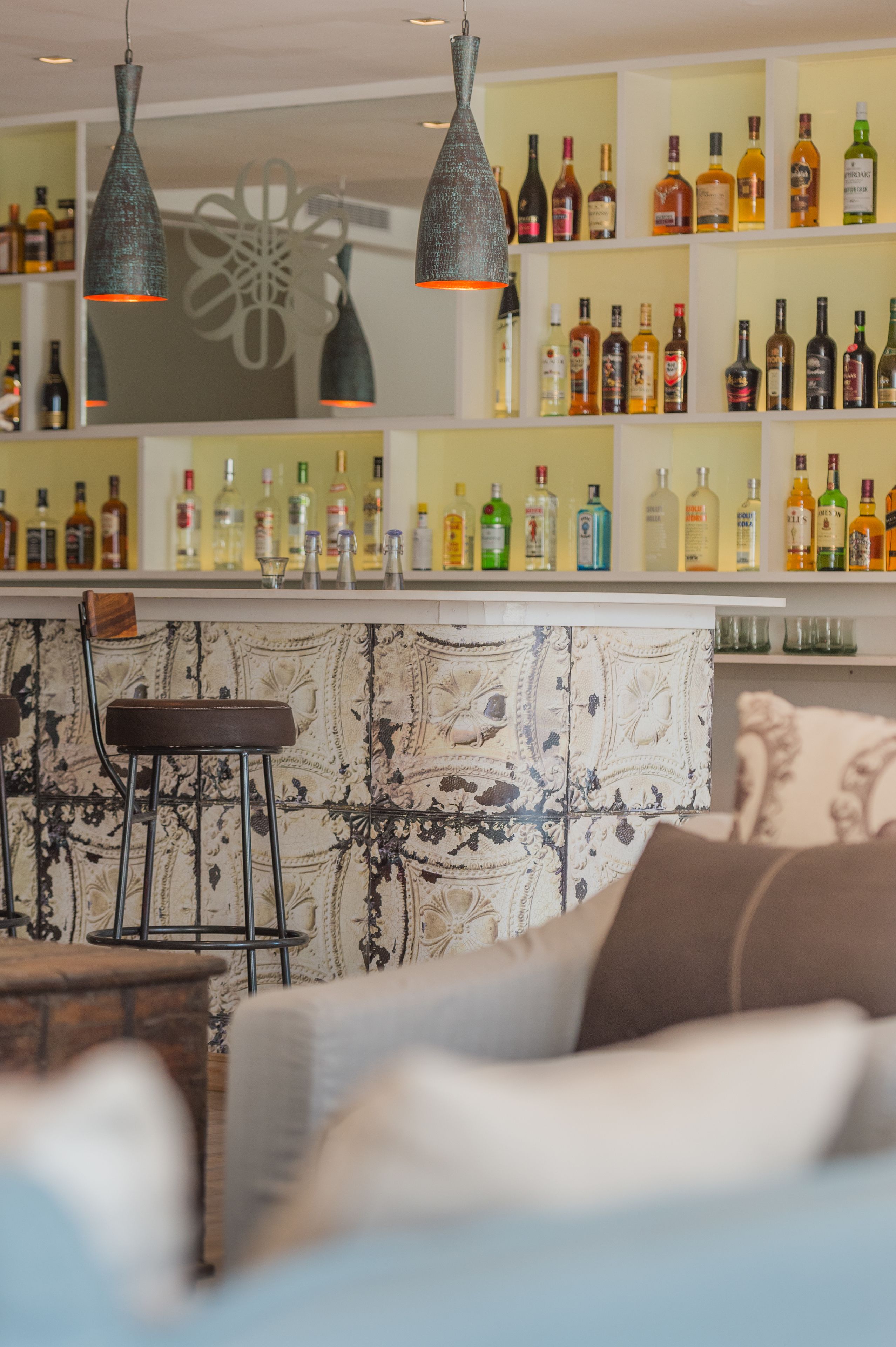 A bar area with a variety of liquor bottles, hanging pendant lights, and a bar counter.