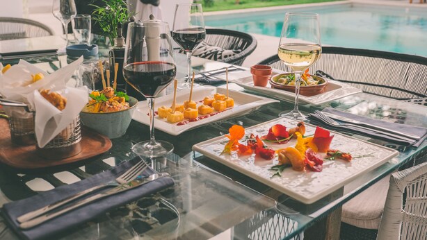 A dining table set with various dishes, glasses of wine, and a view of a swimming pool. - Latitude 15 Degrees (Lusaka)