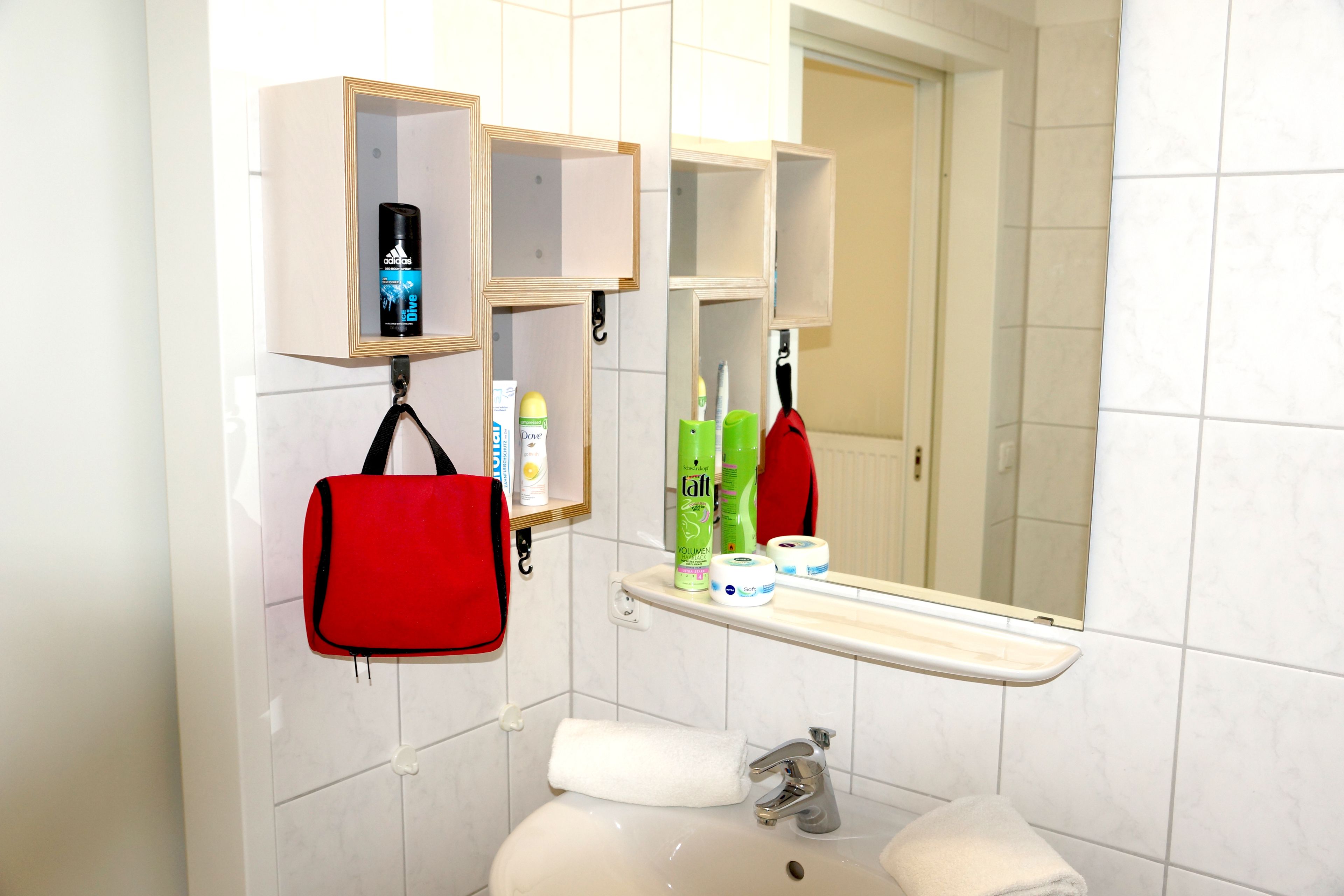 A bathroom with a sink, mirror, and shelves with toiletries.
