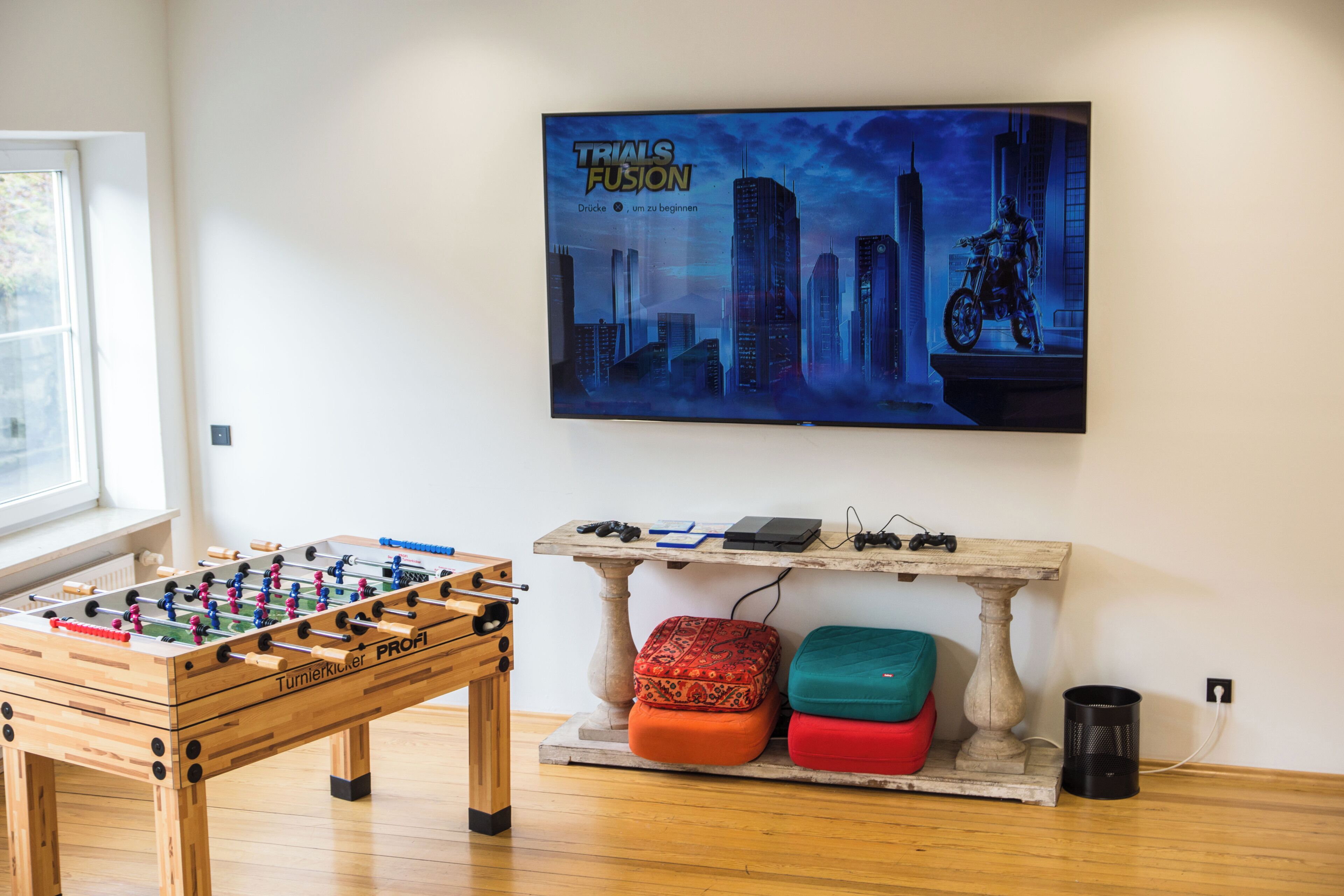 A room with a foosball table, a table with electronic devices, and a poster on the wall.