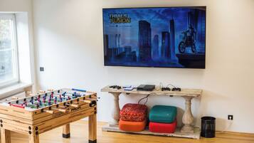 A room with a foosball table, a table with electronic devices, and a poster on the wall.