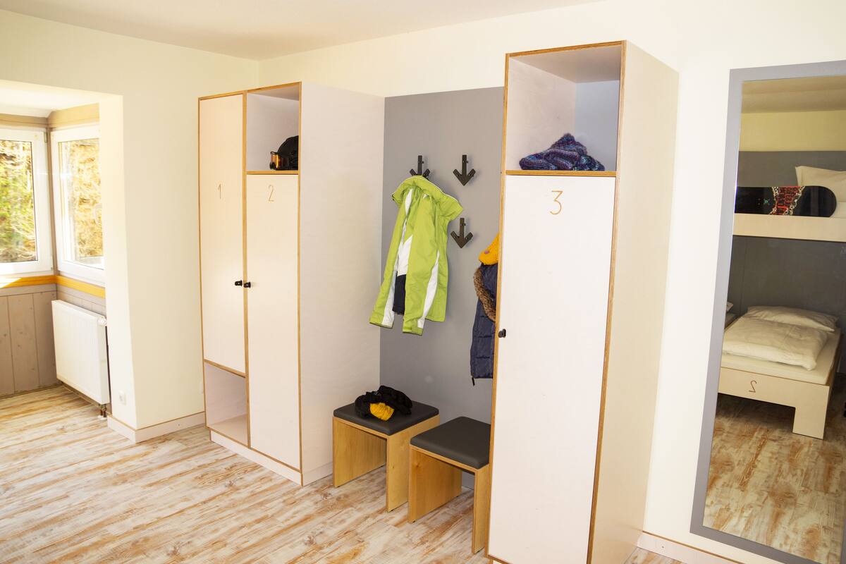 A room with a wooden floor, a window, a bed, and a wardrobe with numbered compartments.