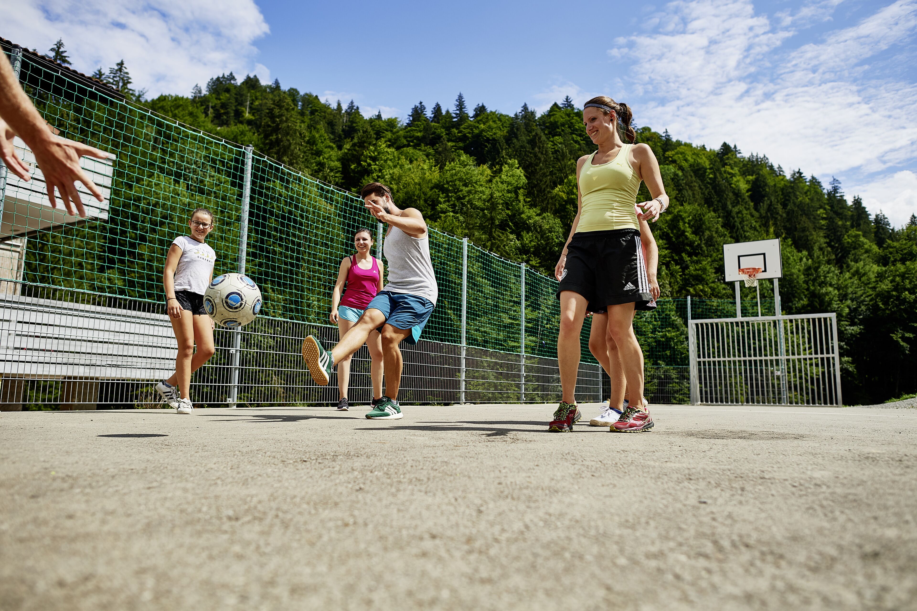 Un grupo de personas jugando al fútbol en una cancha al aire libre, con un aro de baloncesto al fondo.