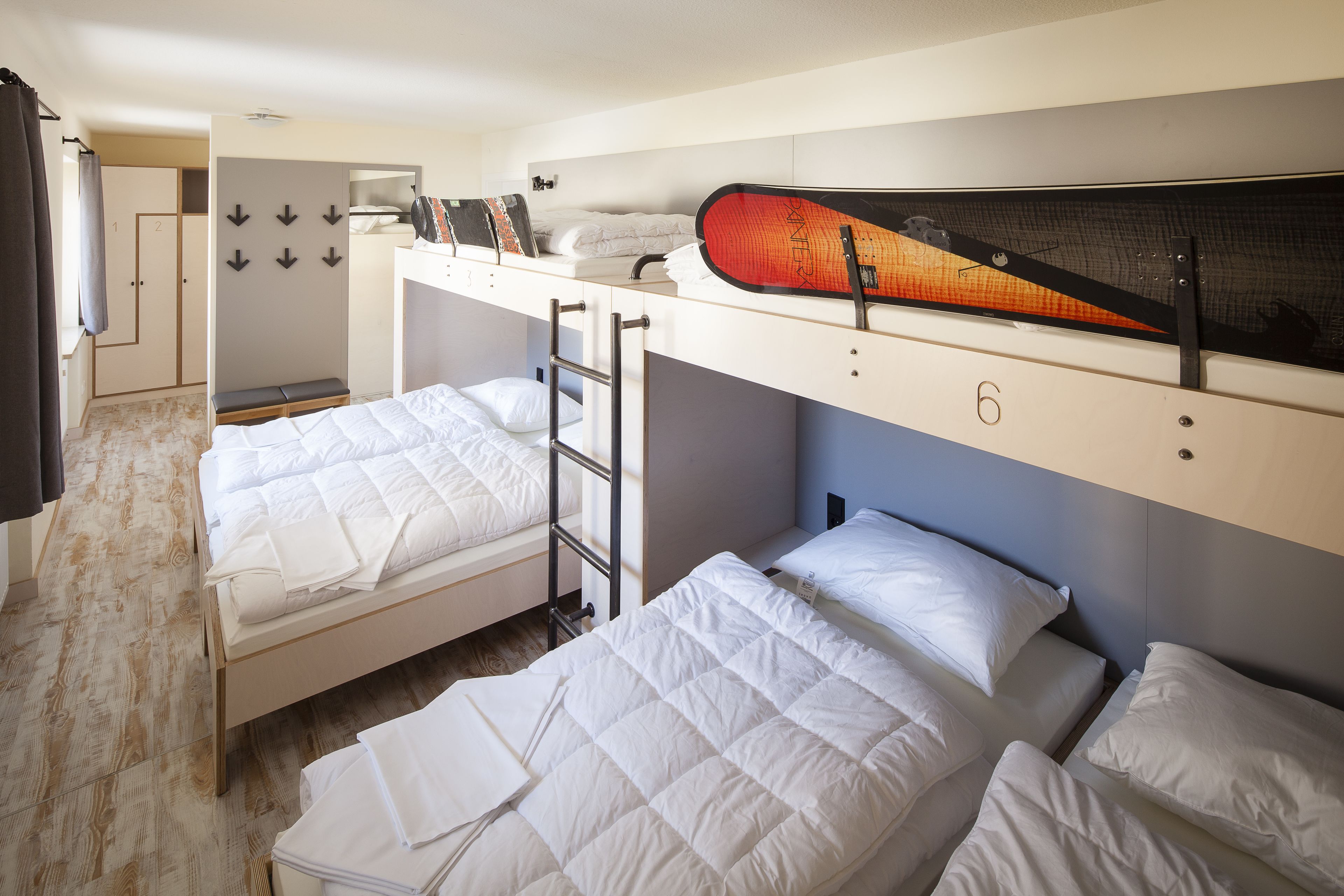 A dormitory room with bunk beds, a ladder, a desk, and a surfboard on the wall.