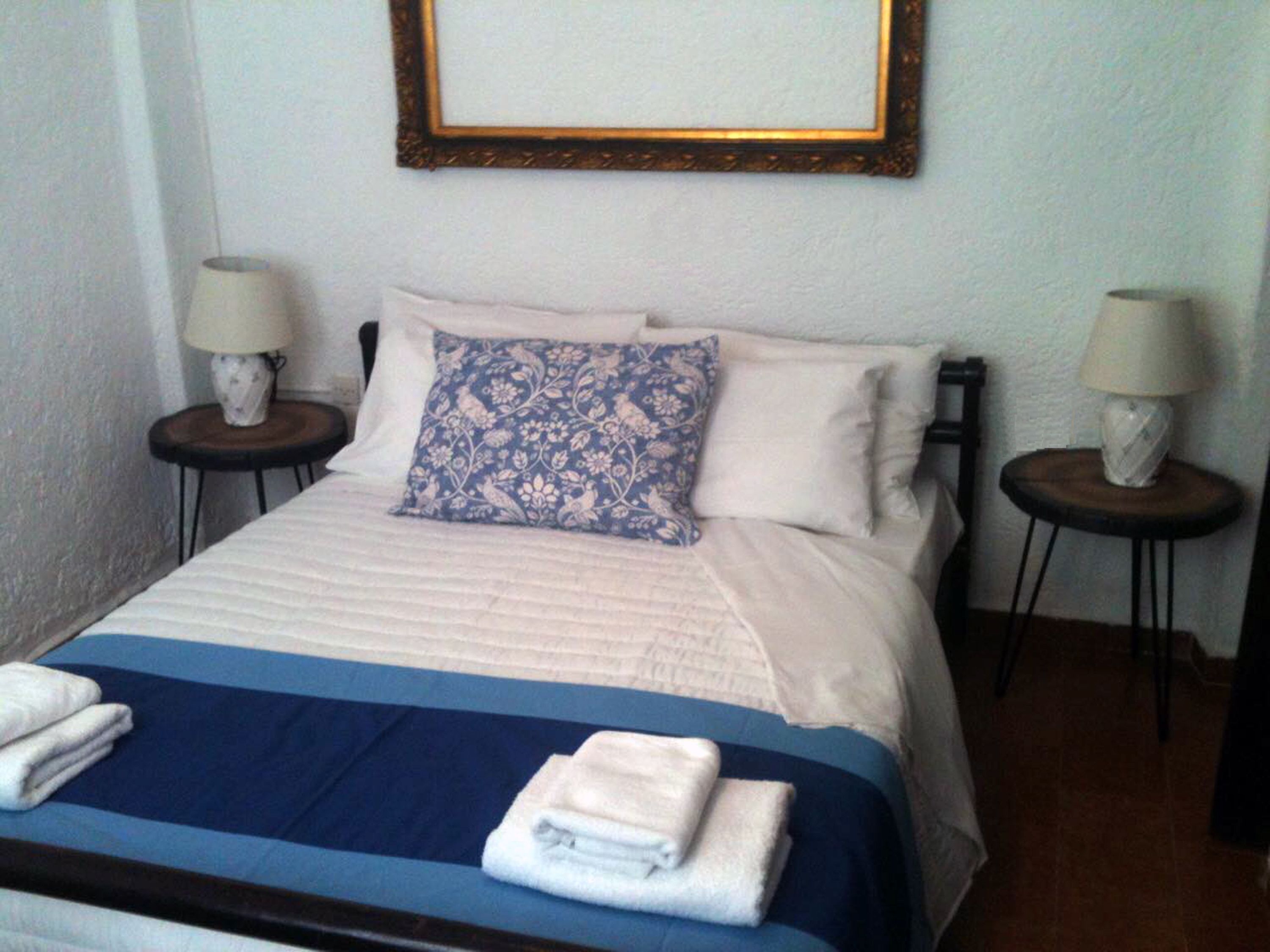 A neatly made bed with a blue and white bedspread, two pillows, and two bedside lamps on matching nightstands.