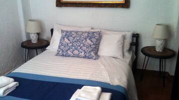 A neatly made bed with a blue and white bedspread, two pillows, and two bedside lamps on matching nightstands.