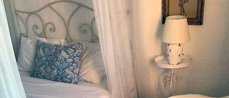 A bedroom with a bed, a bedside table with a lamp, a chair, and a vase of flowers.