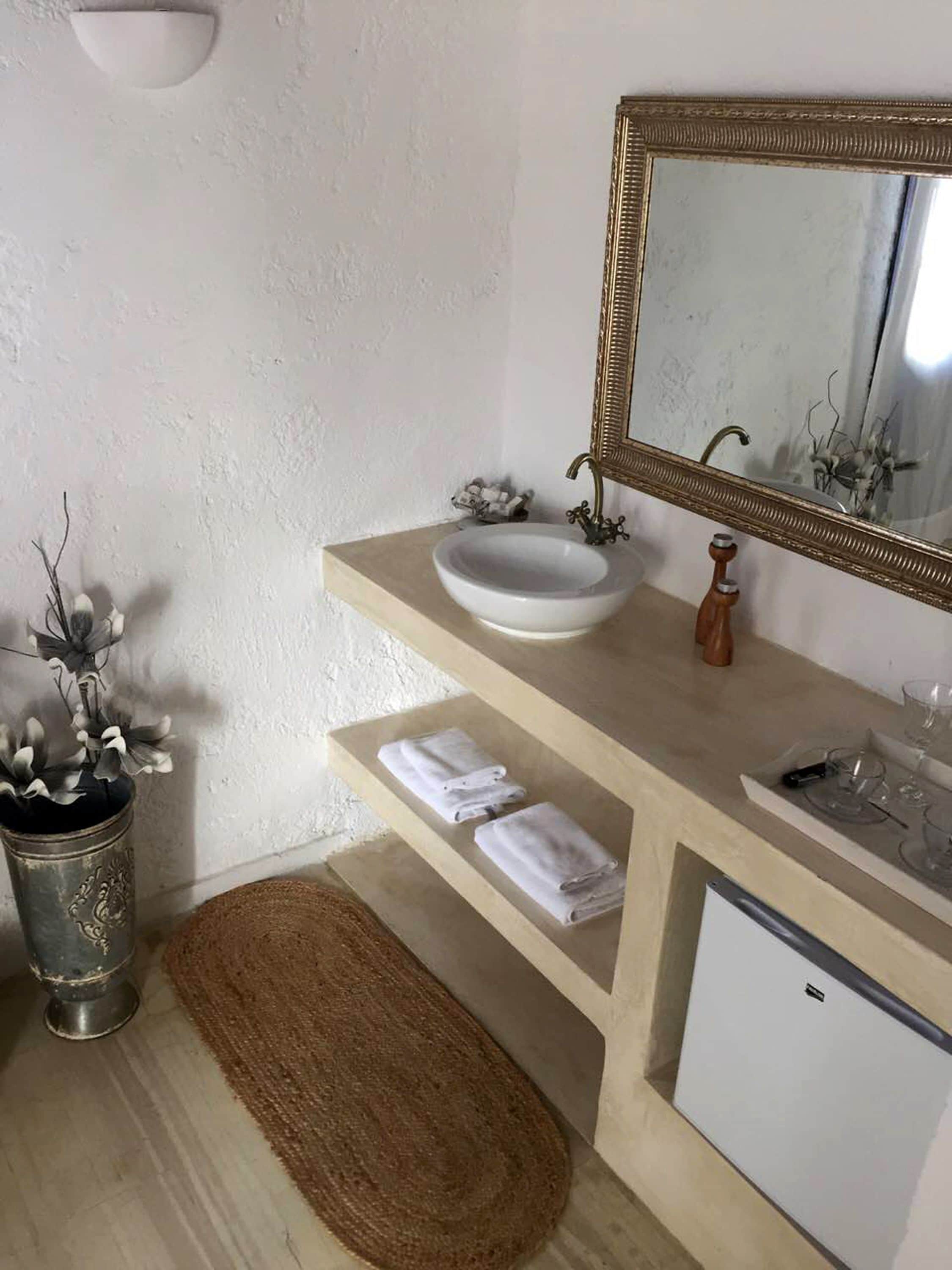 A bathroom with a white sink, a mirror with a gold frame, a towel rack, and a small white cabinet.