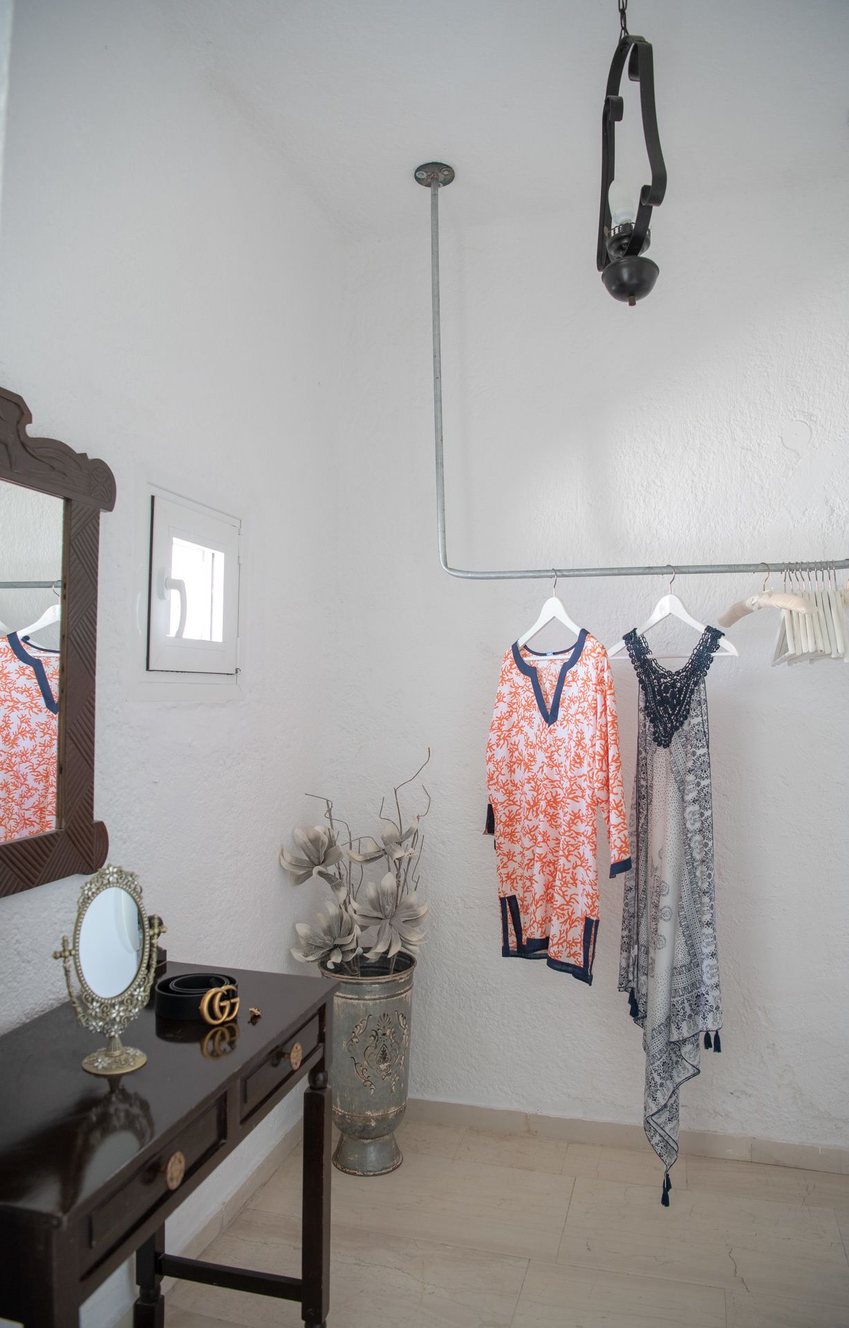 A room with a mirror, a vanity with a Gucci bag, a potted plant, and two hangers with clothing.