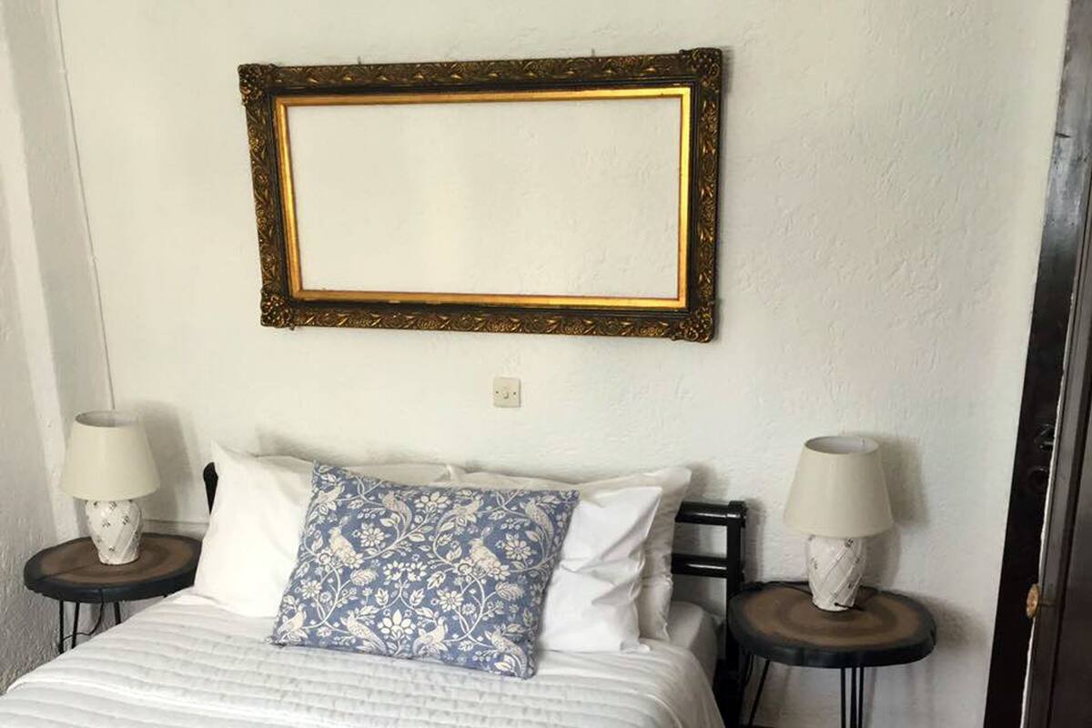 Ein ordentlich eingerichtetes Schlafzimmer mit einem Bett, zwei Nachttischen und einem an der Wand befestigten Spiegel.