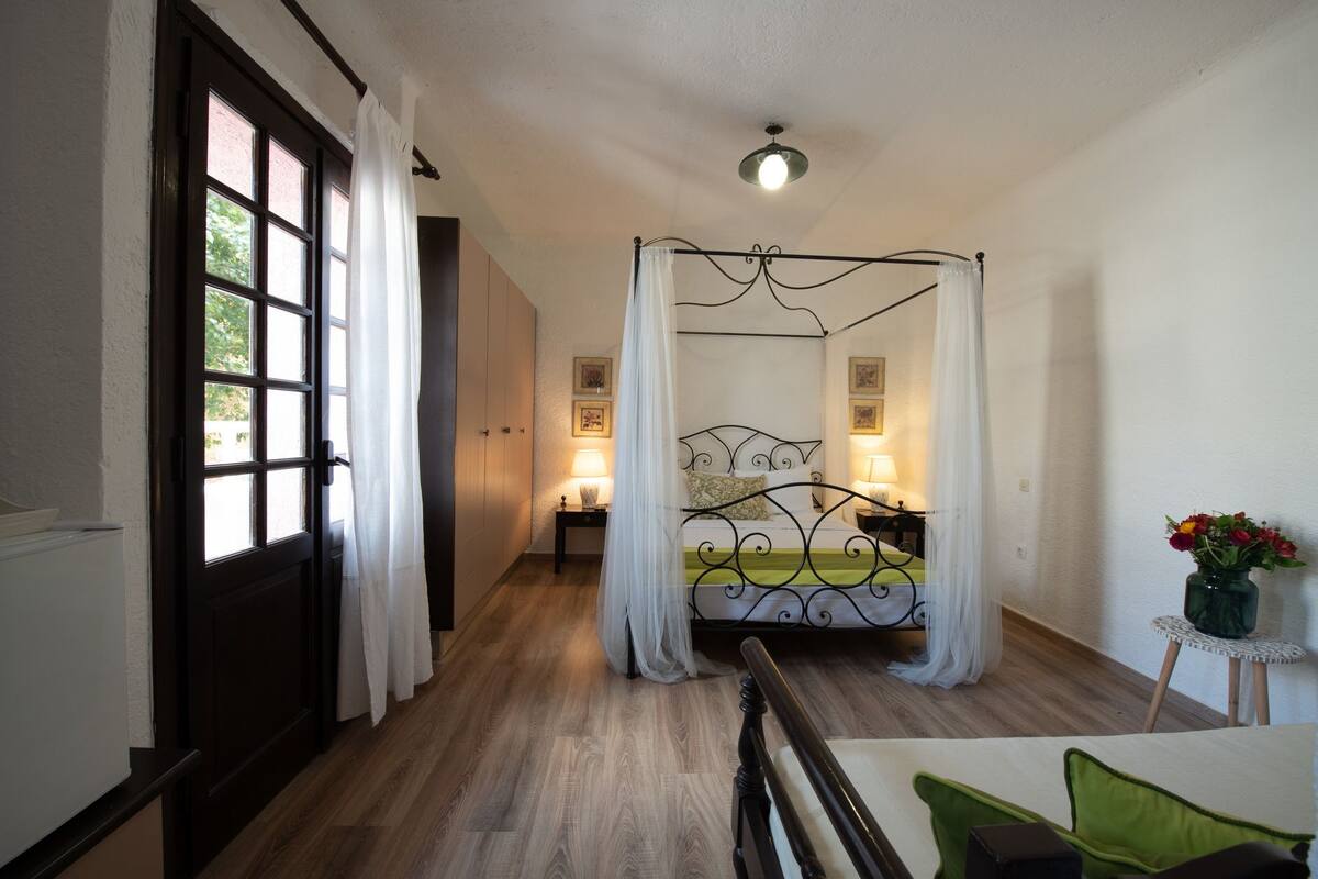 Ein Schlafzimmer mit Himmelbett, Nachttisch mit Lampe und kleinem Tisch mit Blumenvase.