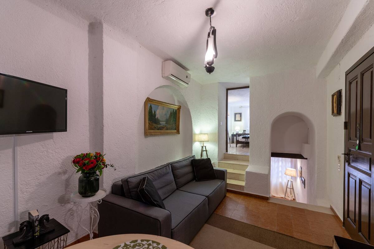 Ein Wohnzimmer mit grauem Sofa, einem Flachbildfernseher, einer Vase mit Blumen und einem Gemälde an der Wand.