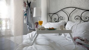 Een netjes opgemaakt bed met witte lakens, een dienblad met croissants, een glas sinaasappelsap en een kop koffie op het bed.