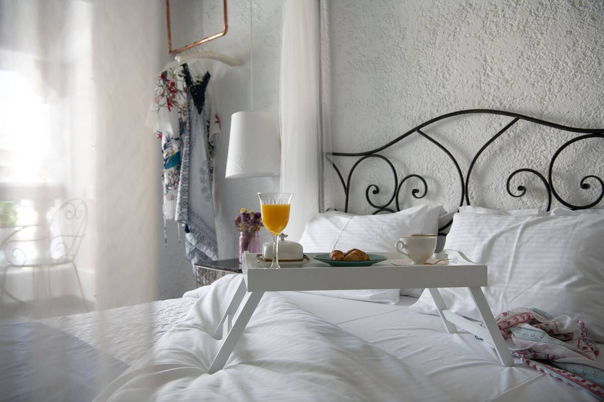 Ein ordentlich bezogenes Bett mit weißen Leinentüchern, ein Tablett mit Croissants, ein Glas Orangensaft und eine Tasse Kaffee auf dem Bett.