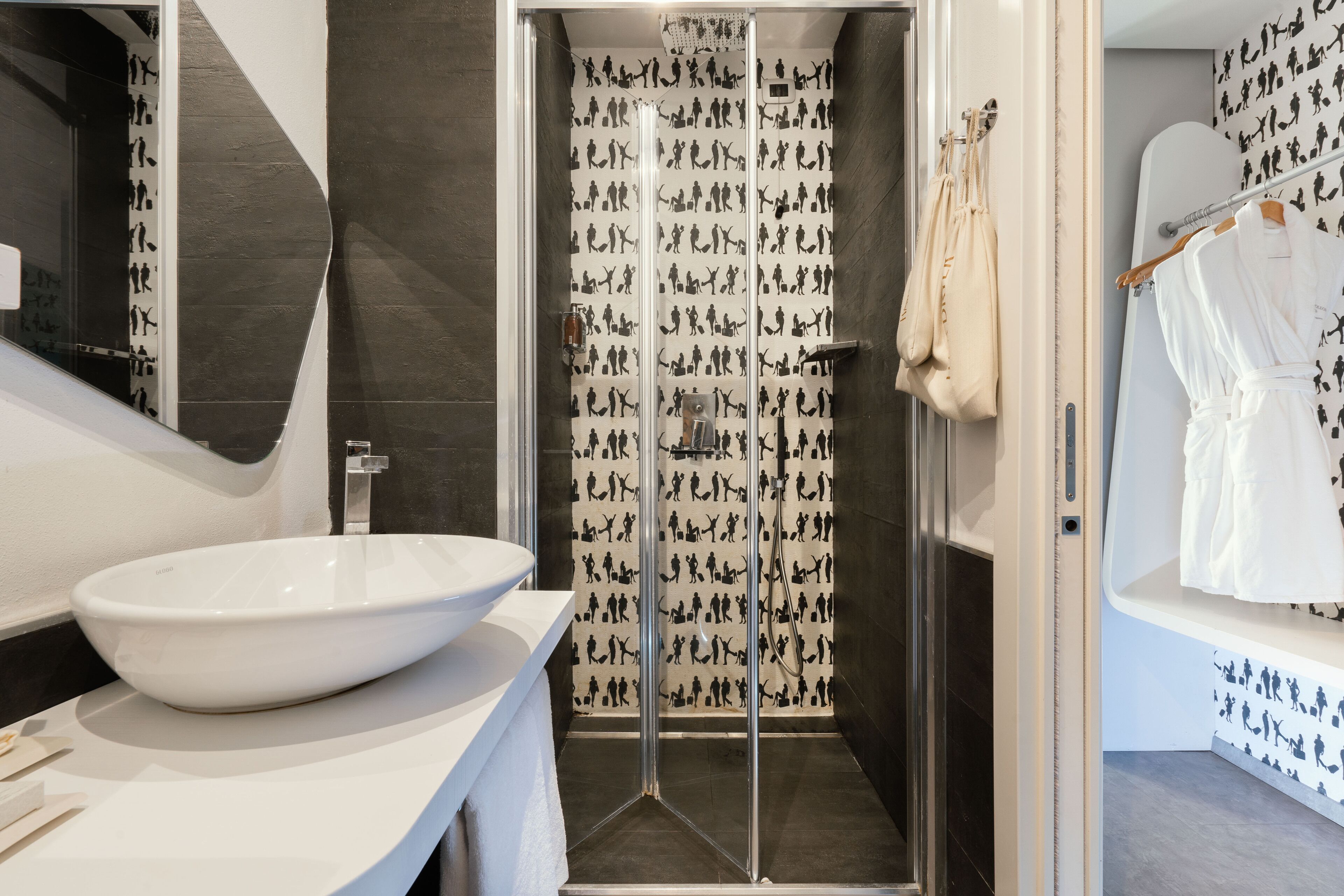 Un bagno moderno con un ampio lavabo bianco, box doccia in vetro e carta da parati decorata.