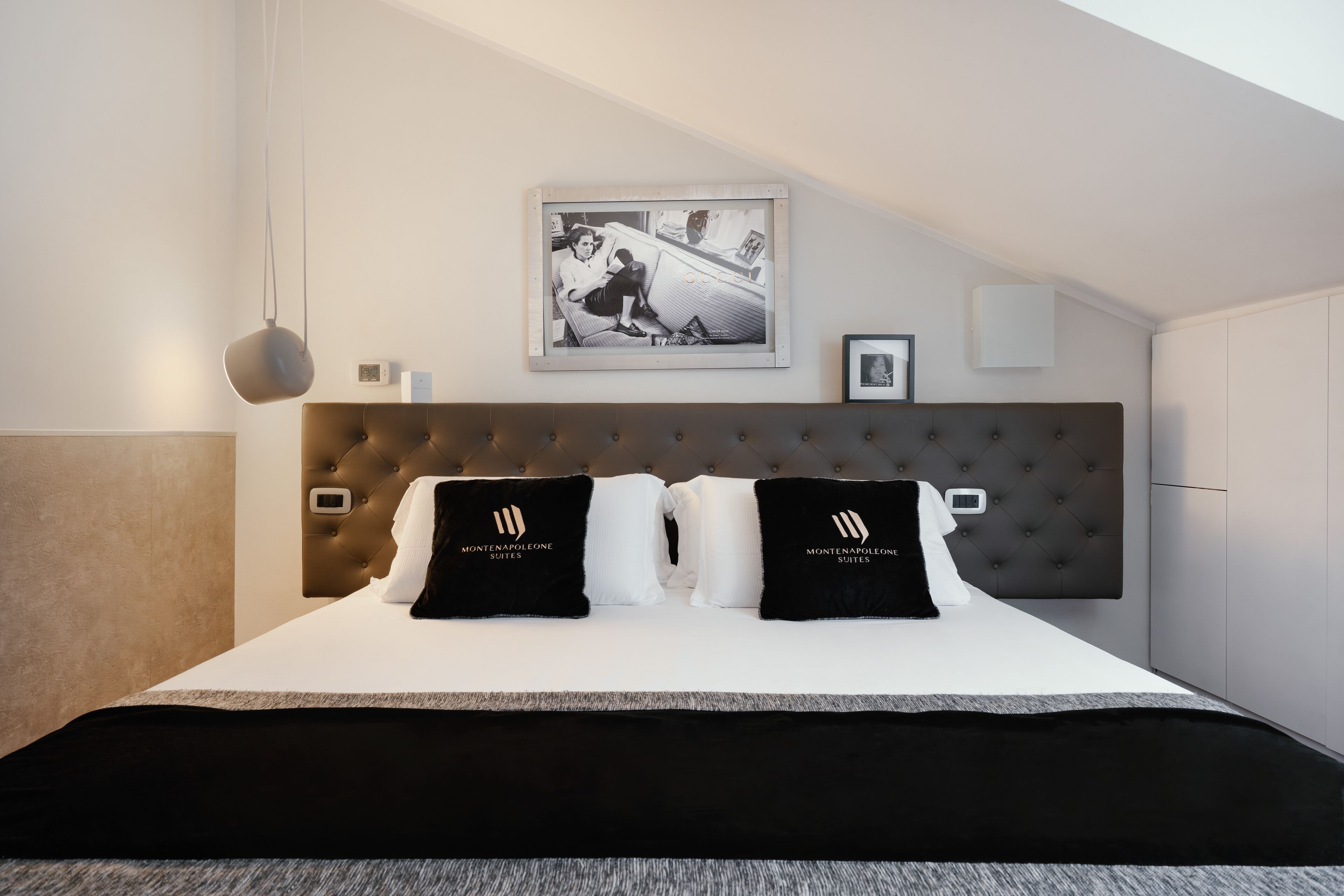 Une chambre d’hôtel moderne avec une tête de lit capitonnée, un grand lit avec une literie noire et blanche, et un tableau encadré au mur.