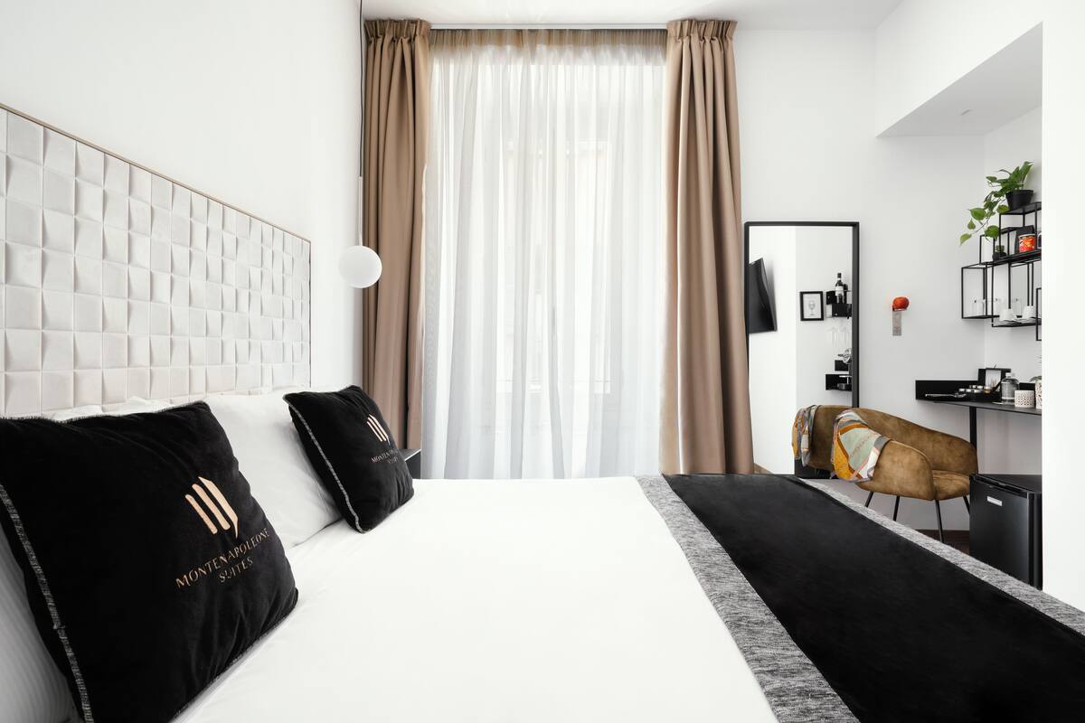 Una habitación de hotel moderna con una cama grande, un cabecero con diseño geométrico, un escritorio con una silla y una pequeña planta en la pared.