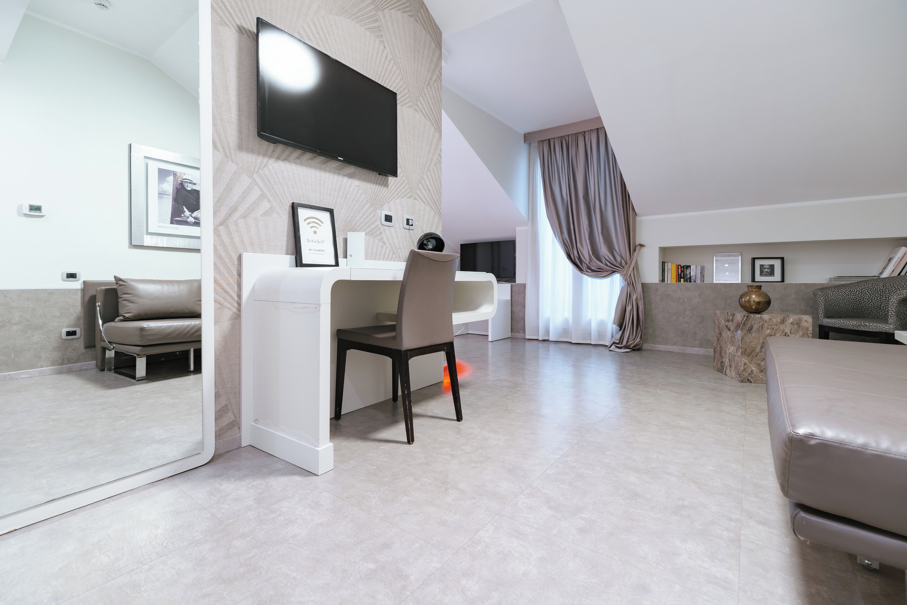 Una habitación de hotel moderna con una cama grande, un escritorio con silla, un televisor de pantalla plana en la pared y un espejo amplio.