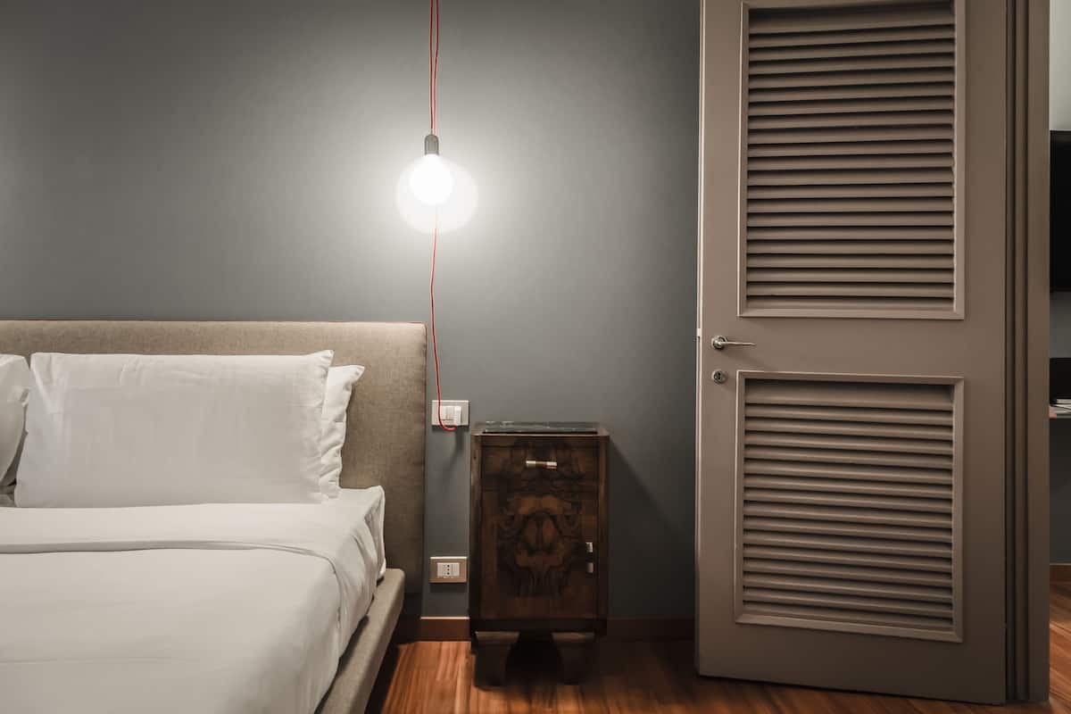 Un dormitorio con cama, mesita de noche y una puerta con paneles verticales.