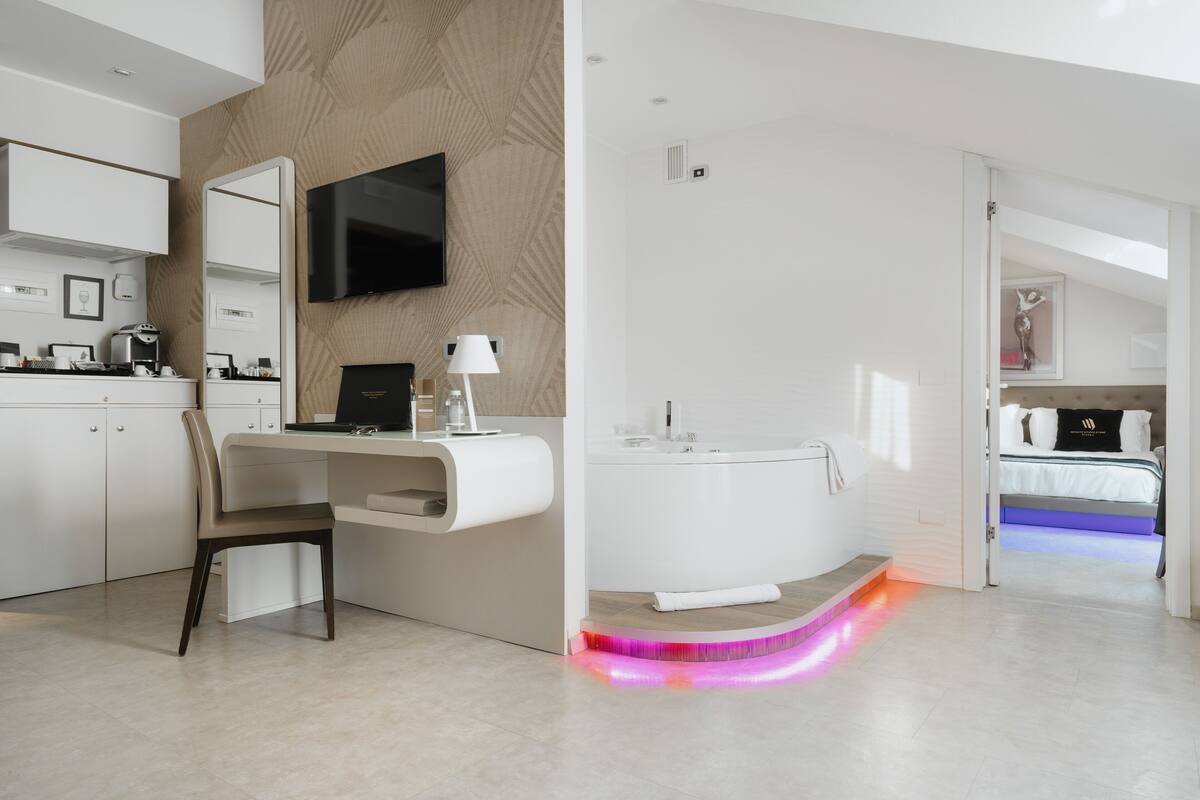 Una habitación de hotel moderna con escritorio, silla, televisor de pantalla plana y una bañera grande con iluminación LED.