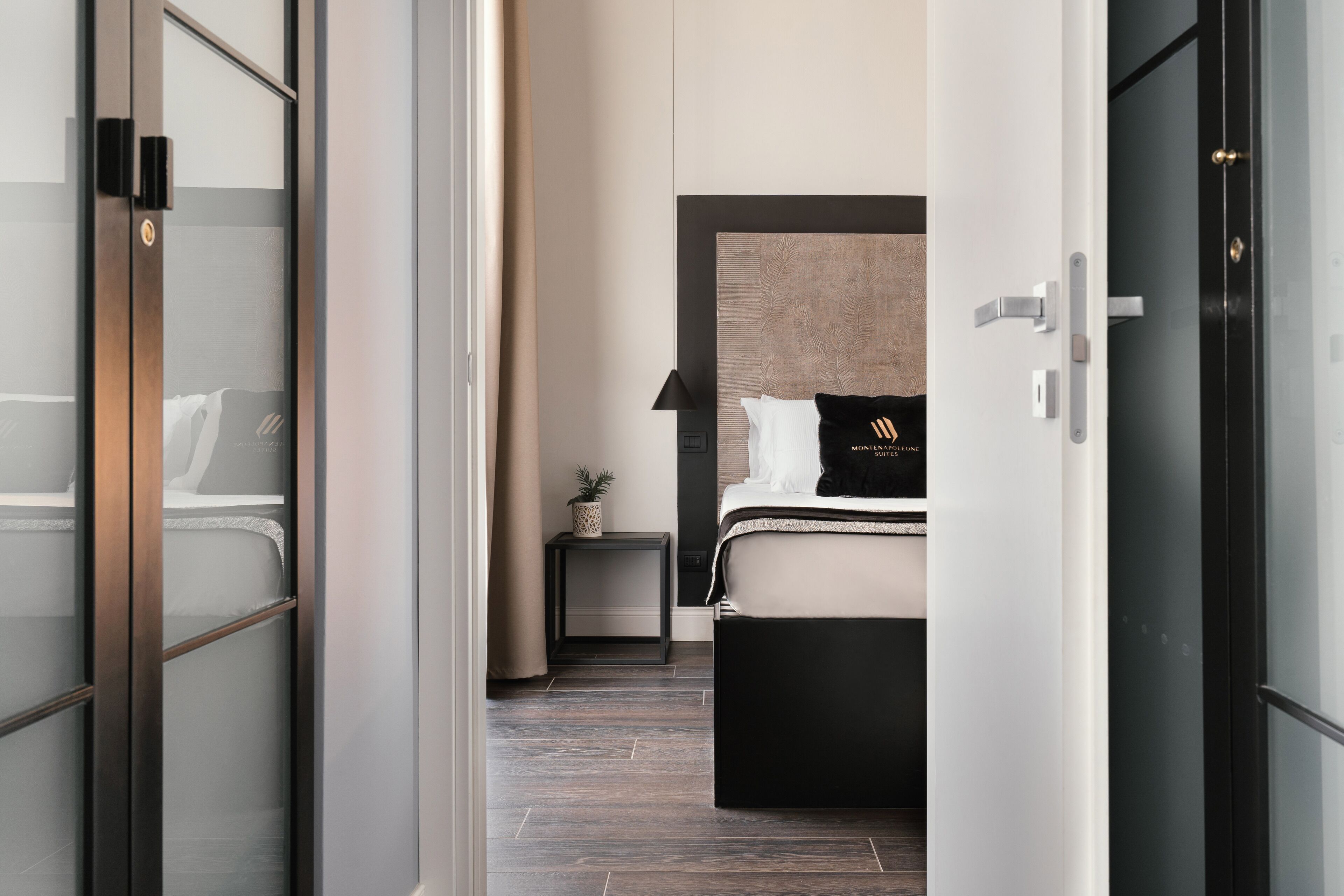 A modern hotel room with a bed, bedside table, lamp, and a small potted plant.