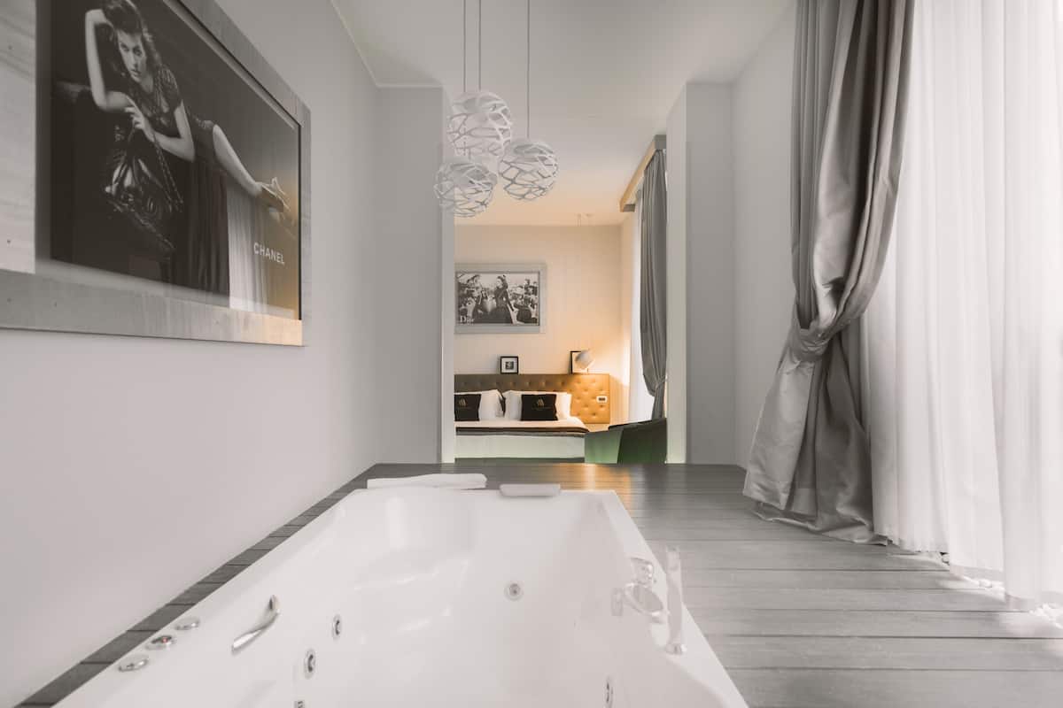 Un baño moderno con una bañera grande, ducha y retrete. En el fondo, se ve una cama con cabecera verde.