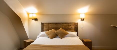 A neatly made bed with a wooden headboard, two bedside lamps, and a brown throw blanket.