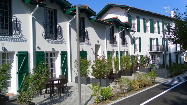 A white building with green shutters and balconies, outdoor seating, and a clear sky. - Hôtel-Résidence Alaia (Ascain)