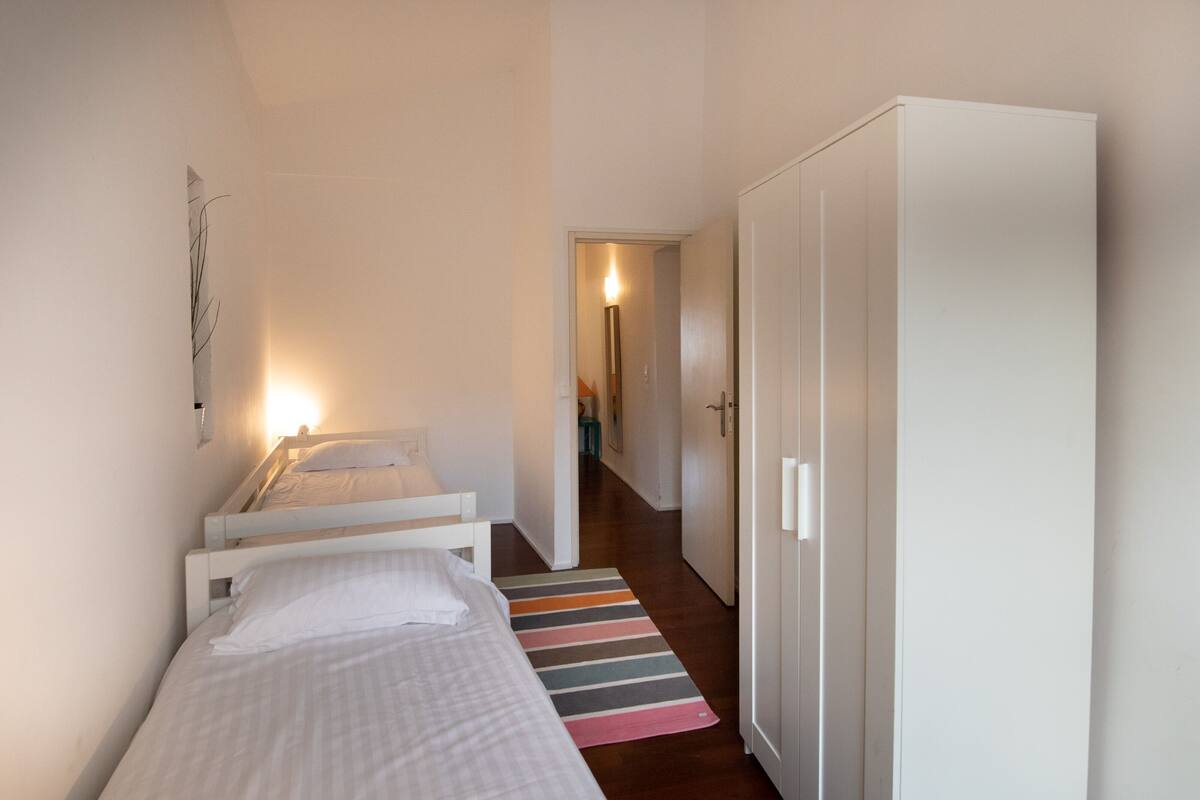 A bedroom with a bed, a wardrobe, and a hallway leading to another room.