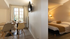 A hotel room with a bed, bedside table, lamp, and a TV mounted on the wall. - Hôtel-Résidence Alaia (Ascain)