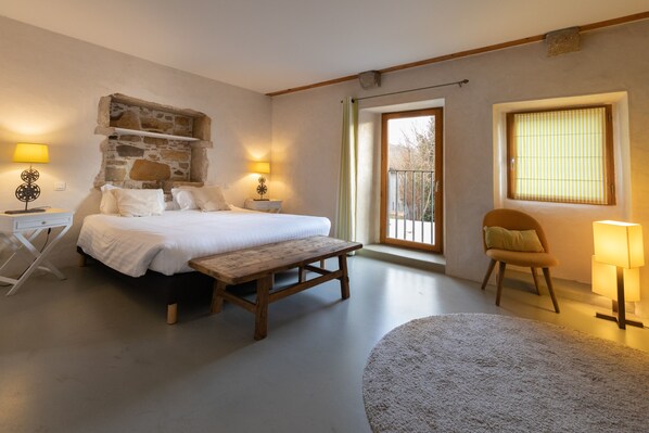 A bedroom with a stone wall, a bed, a bench, a chair, and two bedside lamps.