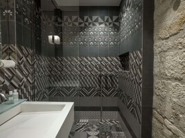 Un baño moderno con baldosas de diseño geométrico, un lavabo blanco y una zona de ducha.