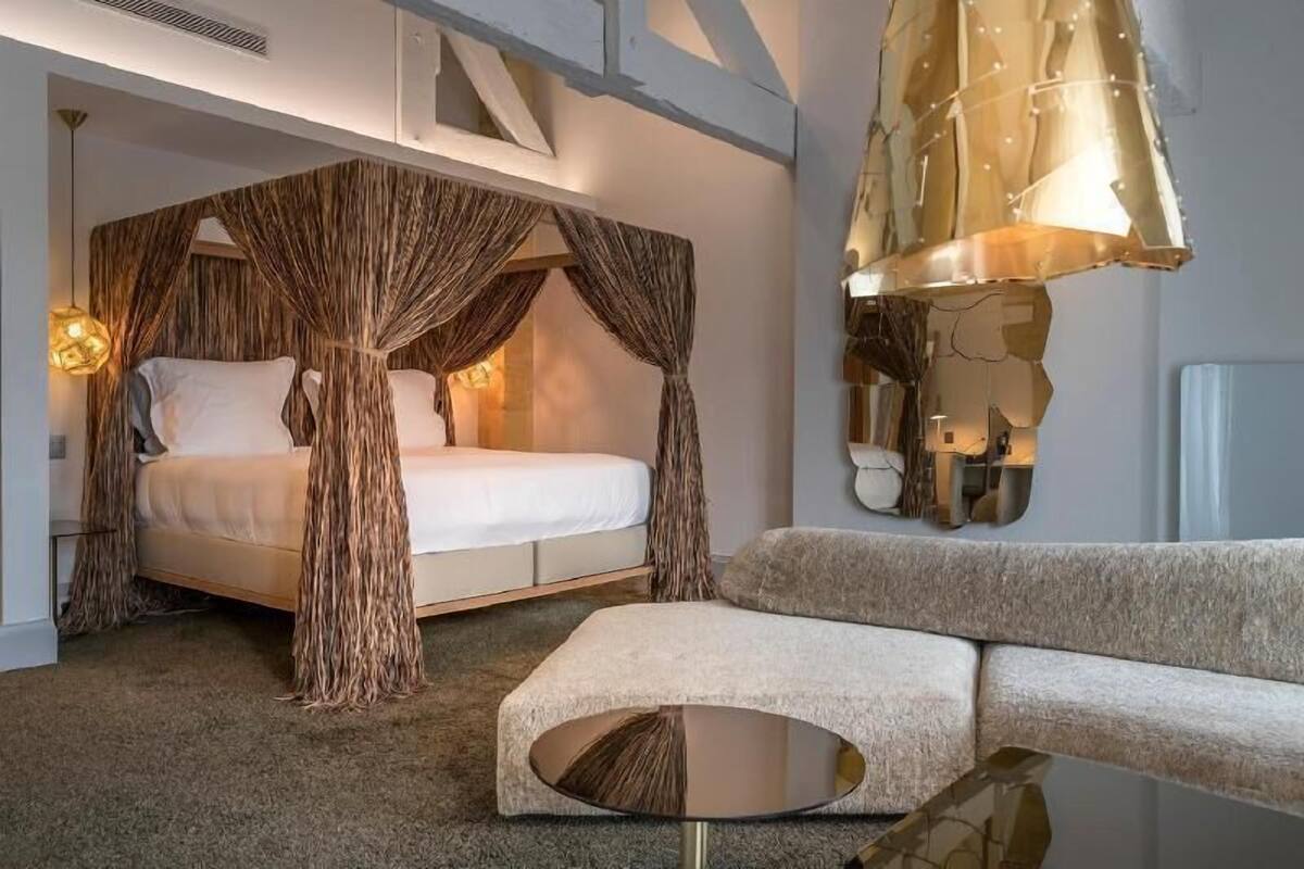 Un dormitorio con cama, sofá, mesa redonda y una lámpara de pared original.