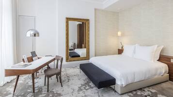 A hotel room with a bed, bedside table, chair, desk, and a large mirror.