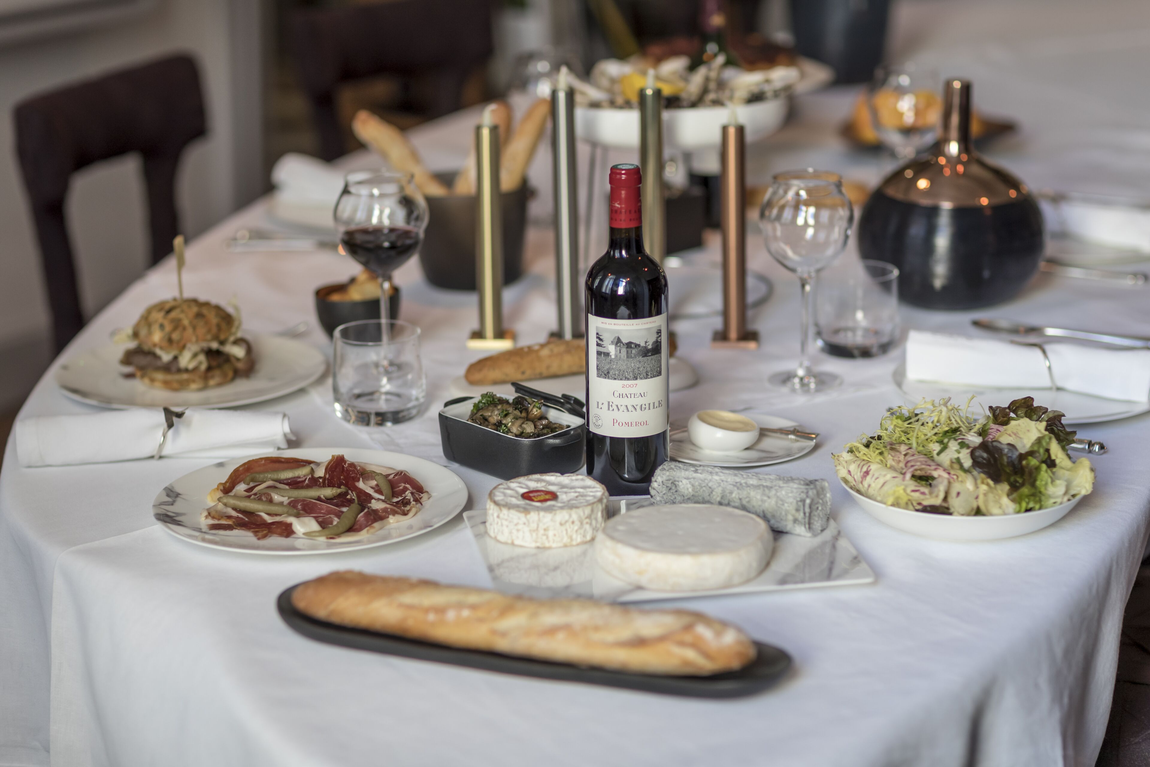 A dining table set with various cheeses, a bottle of wine, and a salad.