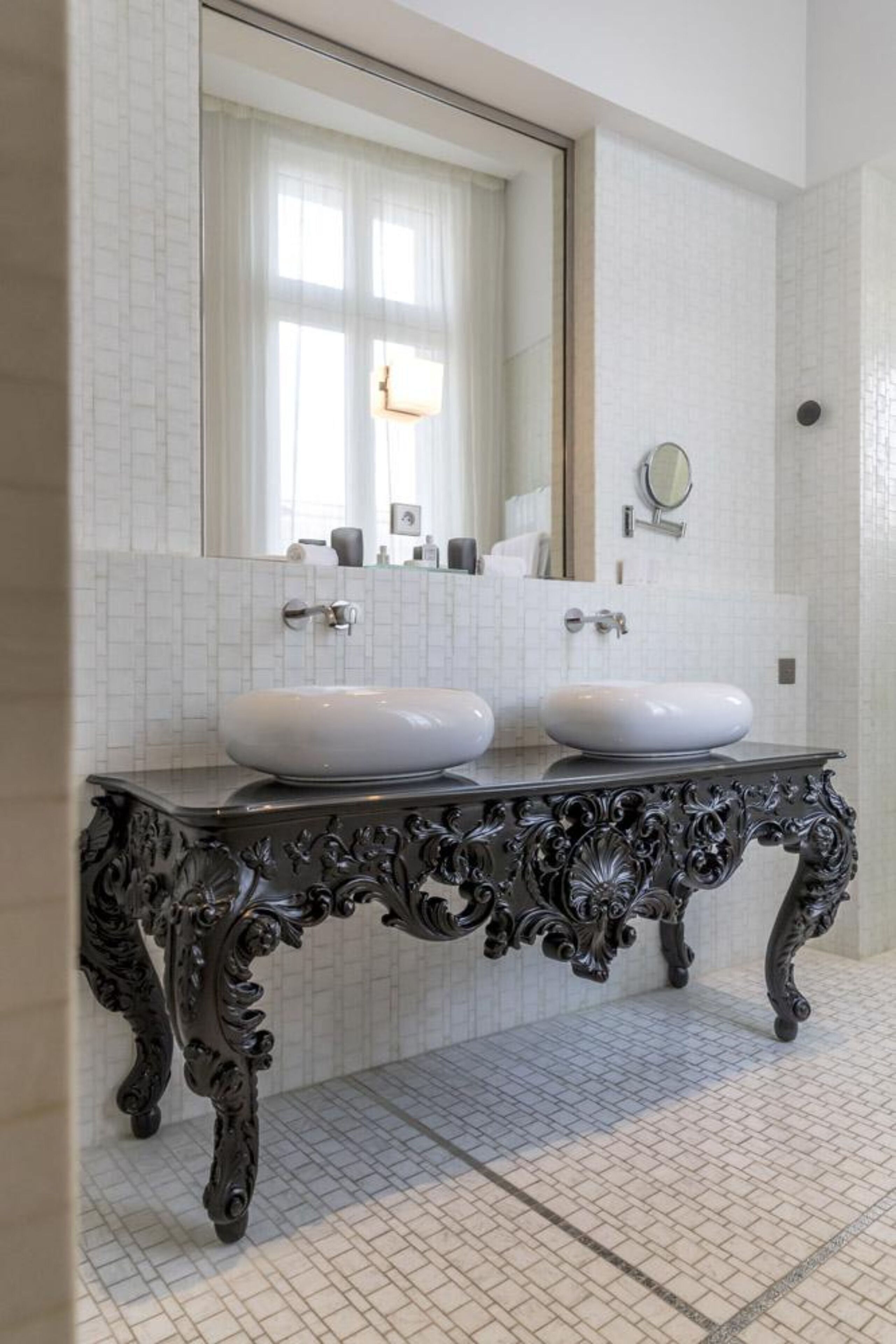 A bathroom with two white sinks, a large mirror, and a decorative black console table.