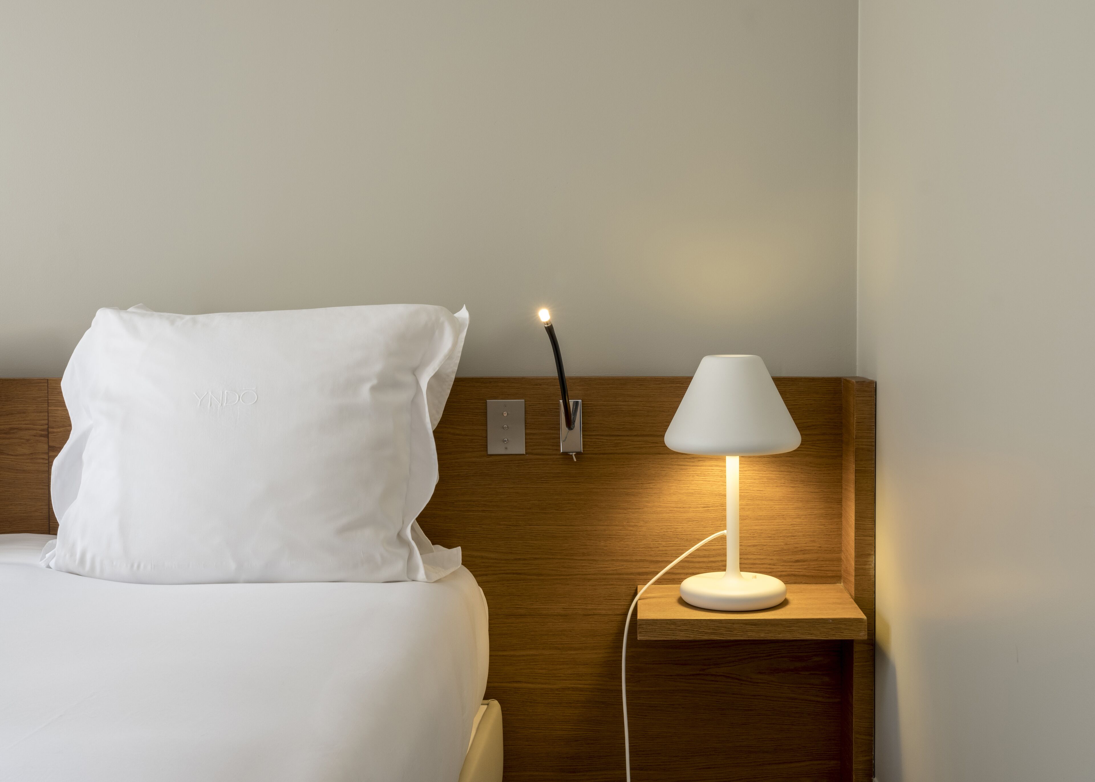 Habitación de hotel con una cama bien hecha, una lámpara de noche y un interruptor de luz en la pared.