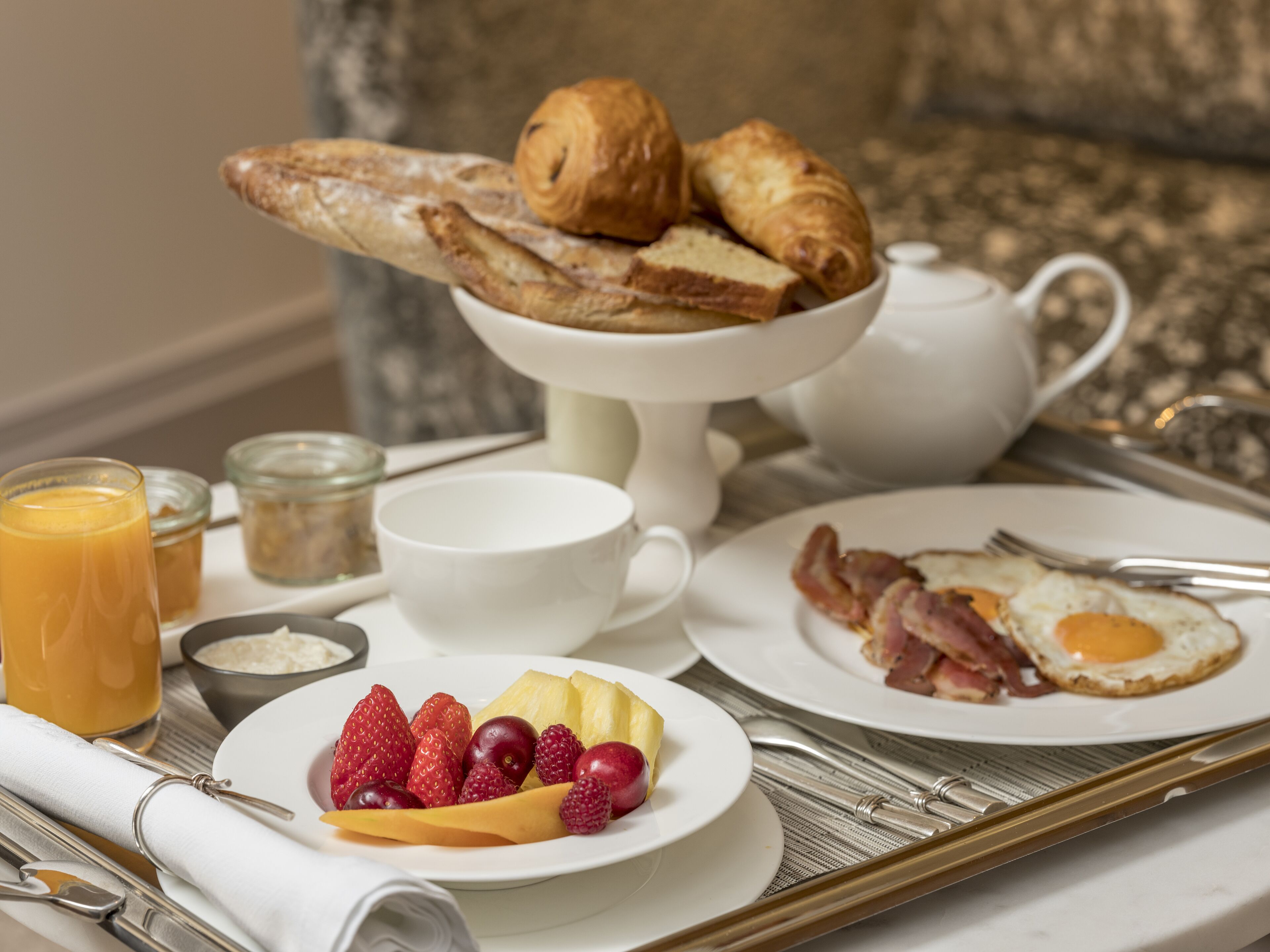 A breakfast tray with croissants, eggs, bacon, strawberries, and a glass of orange juice.