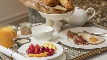 A breakfast tray with croissants, eggs, bacon, strawberries, and a glass of orange juice.