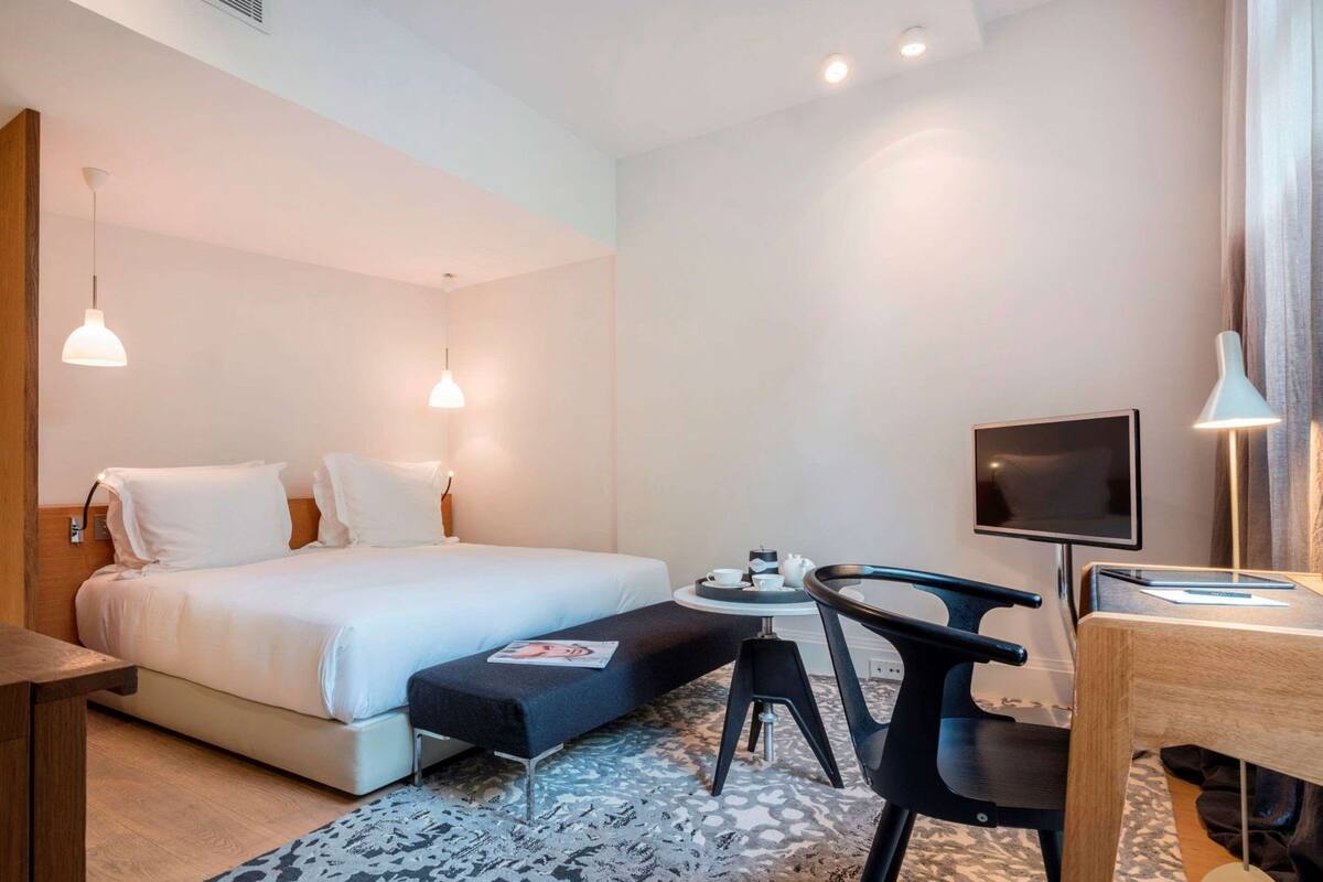 Habitación de hotel con cama, escritorio con silla, televisor y una mesita con una bandeja de objetos.