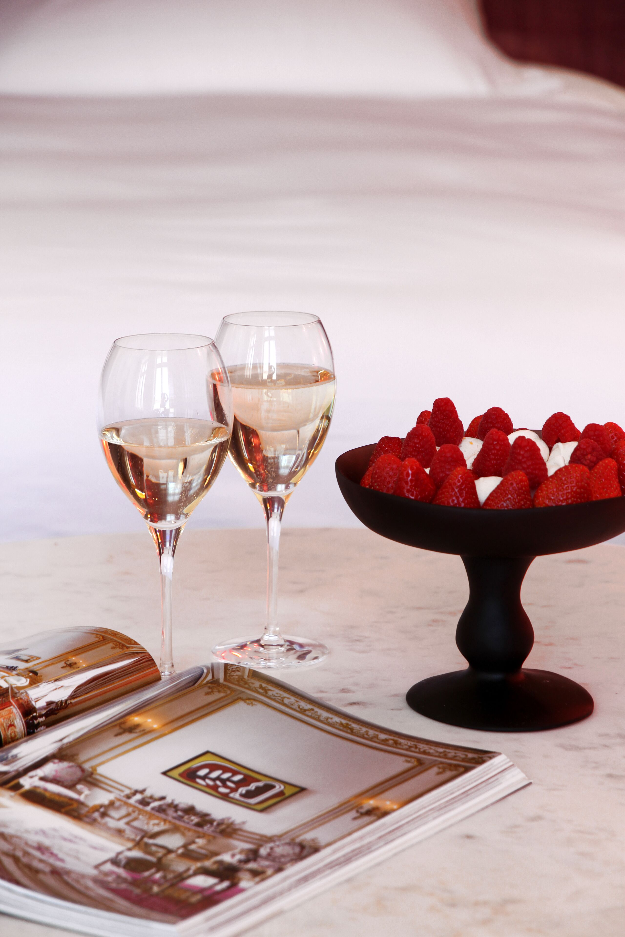Two wine glasses on a table with a bowl of strawberries.