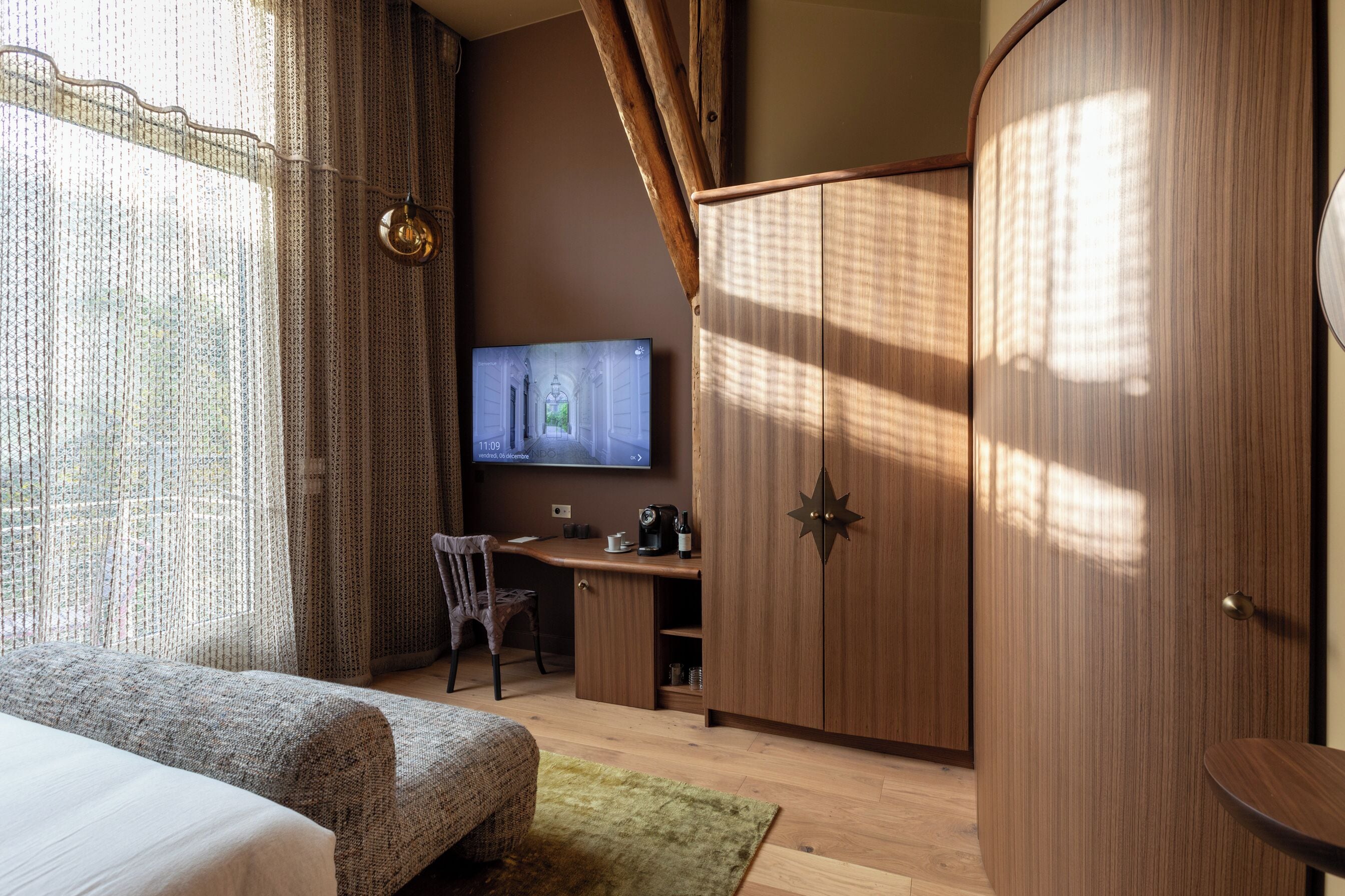 A hotel room with a bed, a desk, a chair, and a wardrobe.