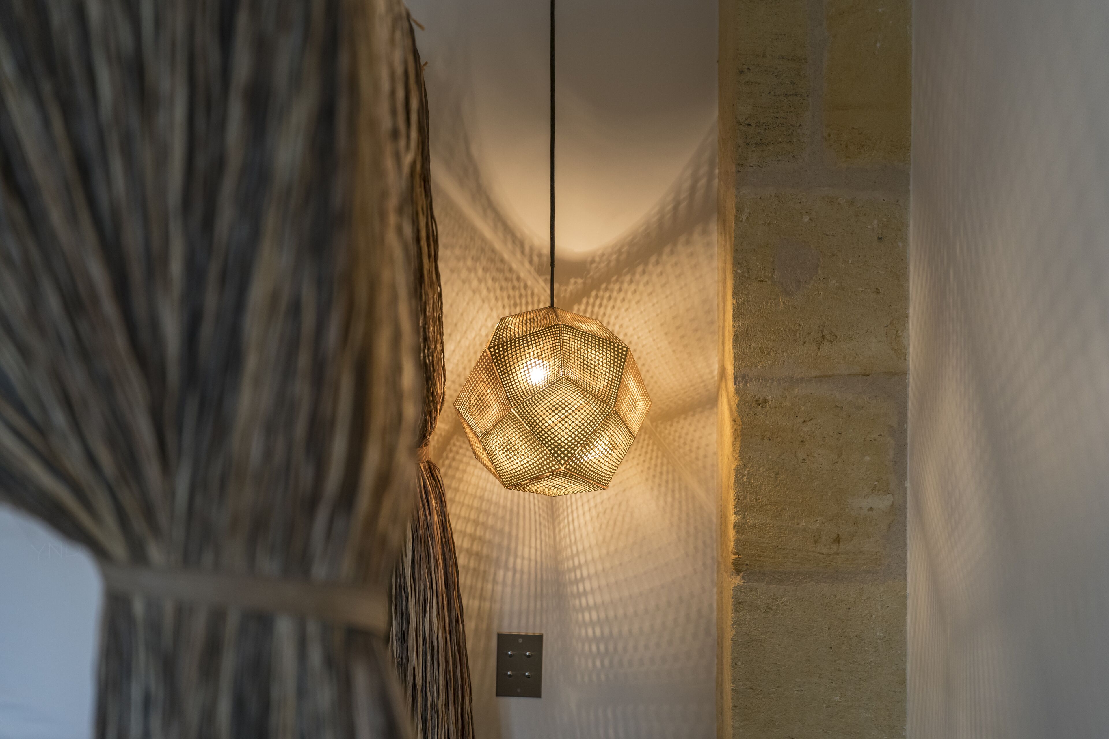 A room with a hanging woven light fixture and a stone wall.
