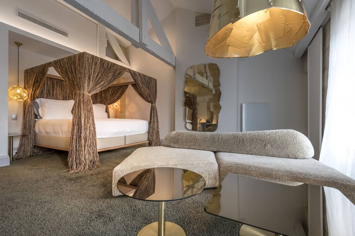 Un dormitorio moderno con una cama con dosel, un sofá, una mesa de centro de vidrio y un espejo grande.