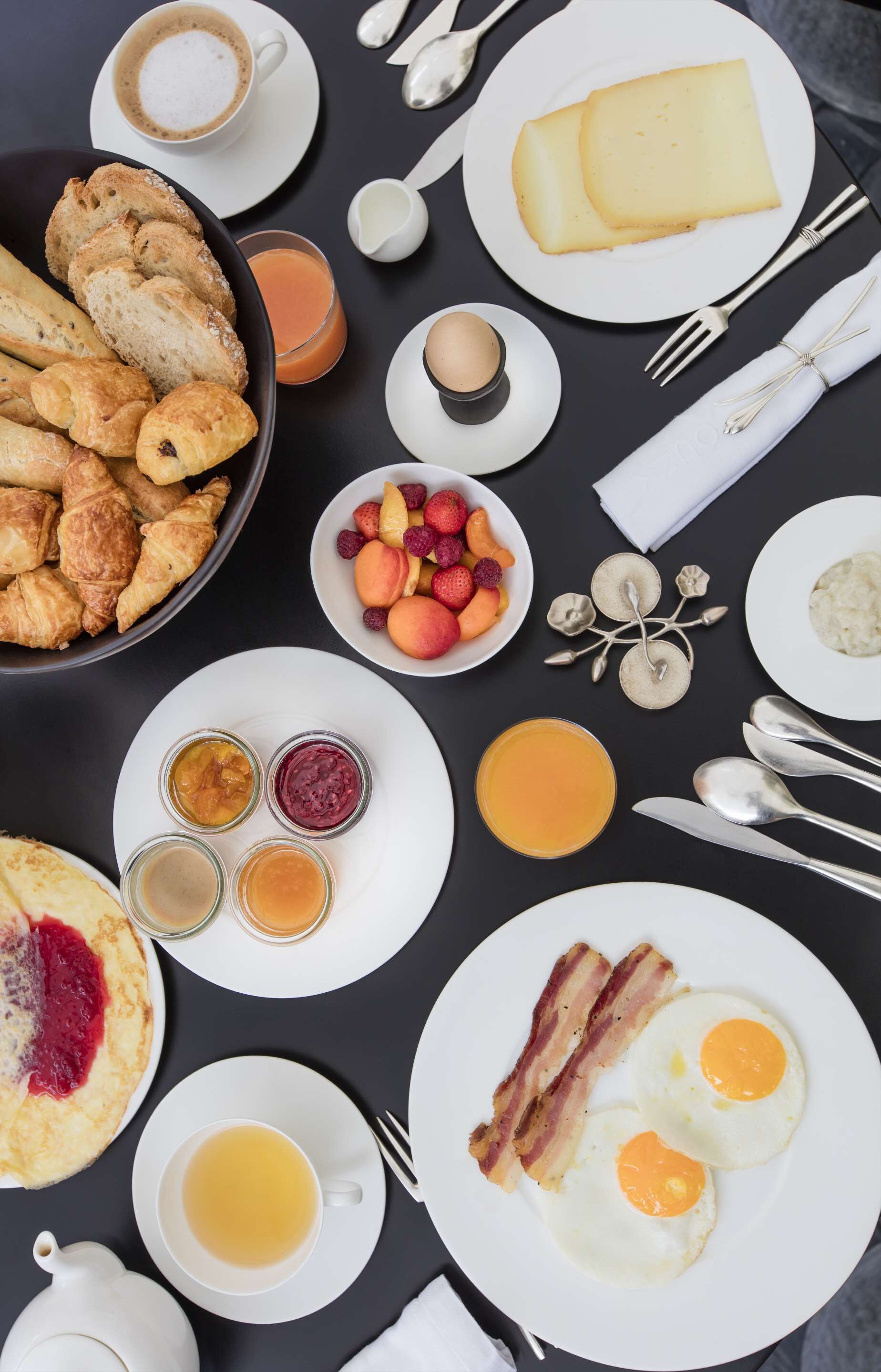 A breakfast spread with croissants, fruit, eggs, and coffee on a table.